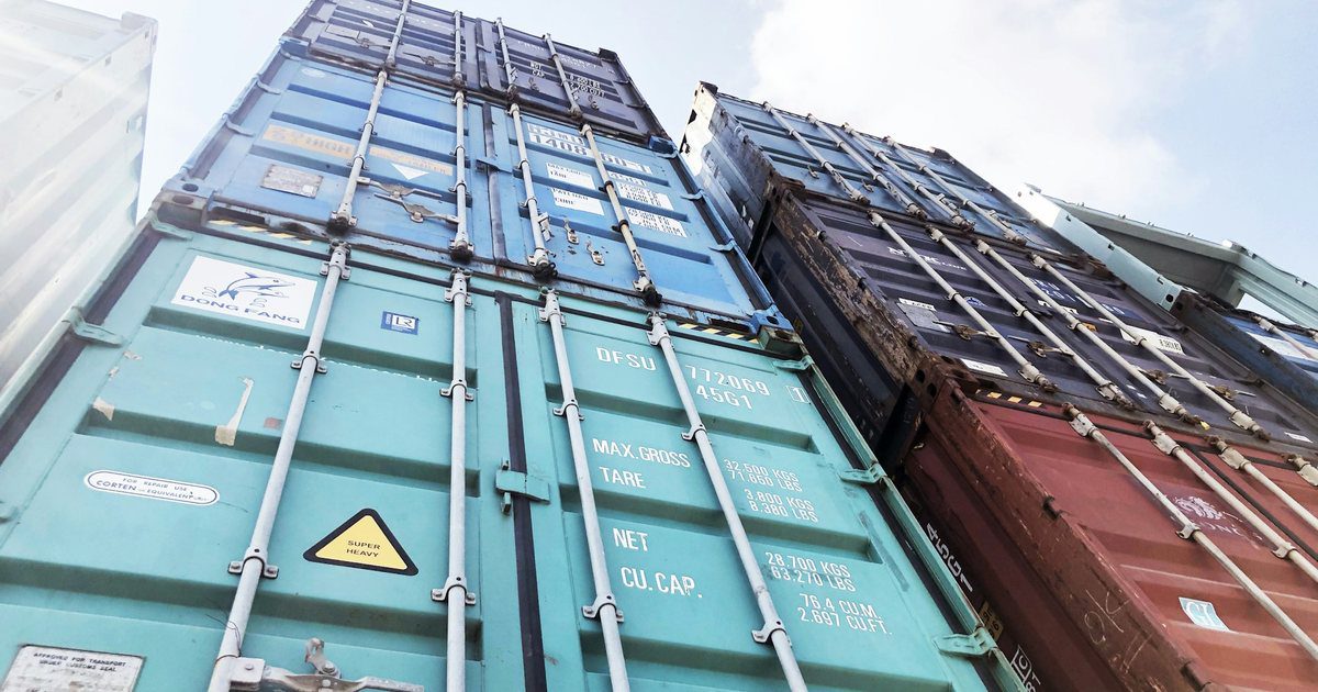 Sealed steel shipping containers stacked at a port terminal under gantry cranes.