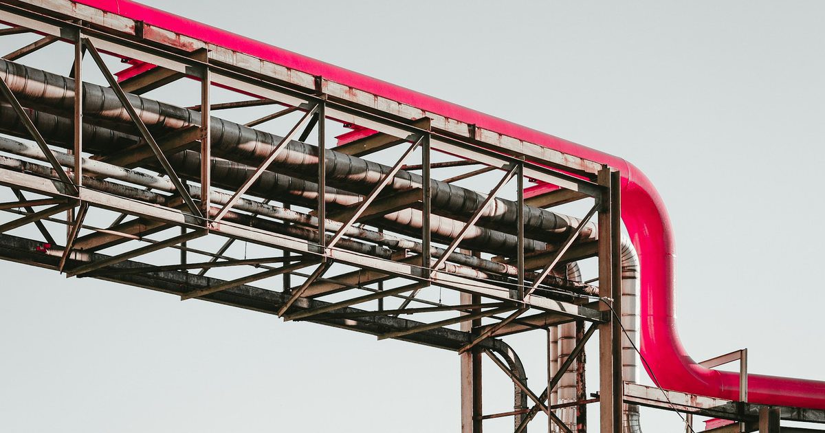 An enclosed industrial conveyor running from open ground straight into the side of a large plant building.