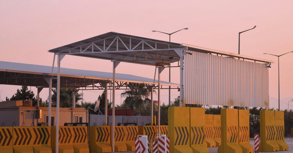 An empty toll plaza with its barrier raised and the roadway continuing straight through the lanes.