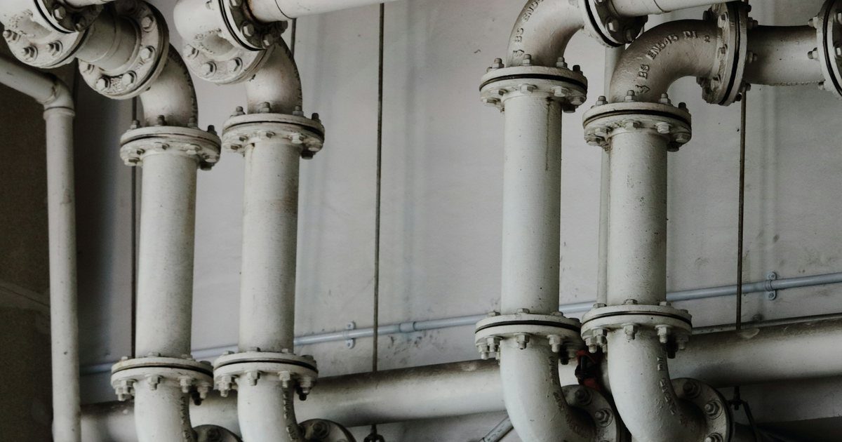 Two identical runs of industrial pipework converging and joining into a single shared manifold.