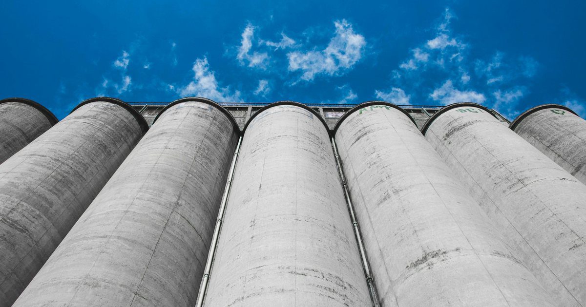 A row of tall sealed concrete storage silos standing under a flat overcast sky.