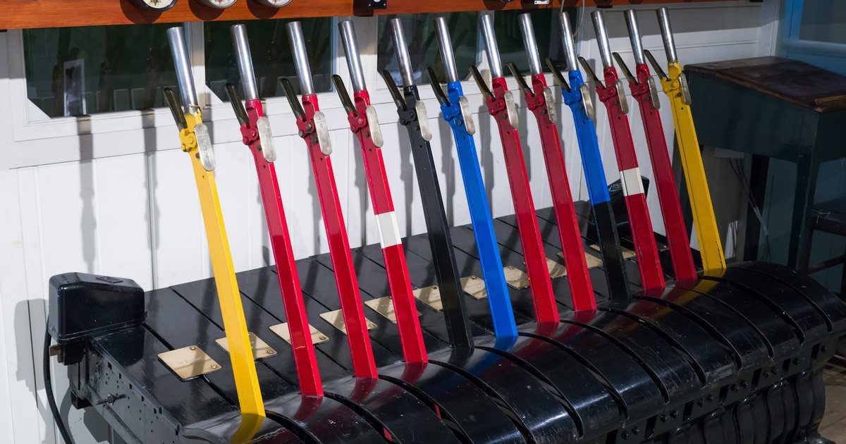 A row of tall painted levers in a railway signal box, one pulled forward out of line with the rest.