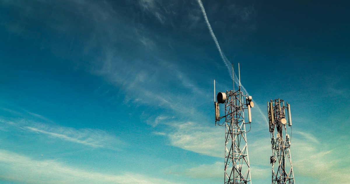 A lattice relay mast on open ground, its drum antennas facing out across distant landscape.