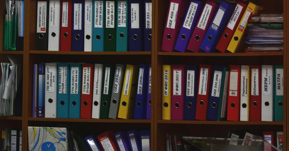 An archive hall of identical shelving rows filled with uniform document boxes, receding down a long aisle.