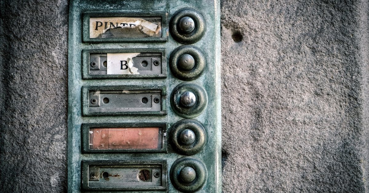 A weathered brushed metal intercom panel filling the frame, with rows of identical worn call buttons.